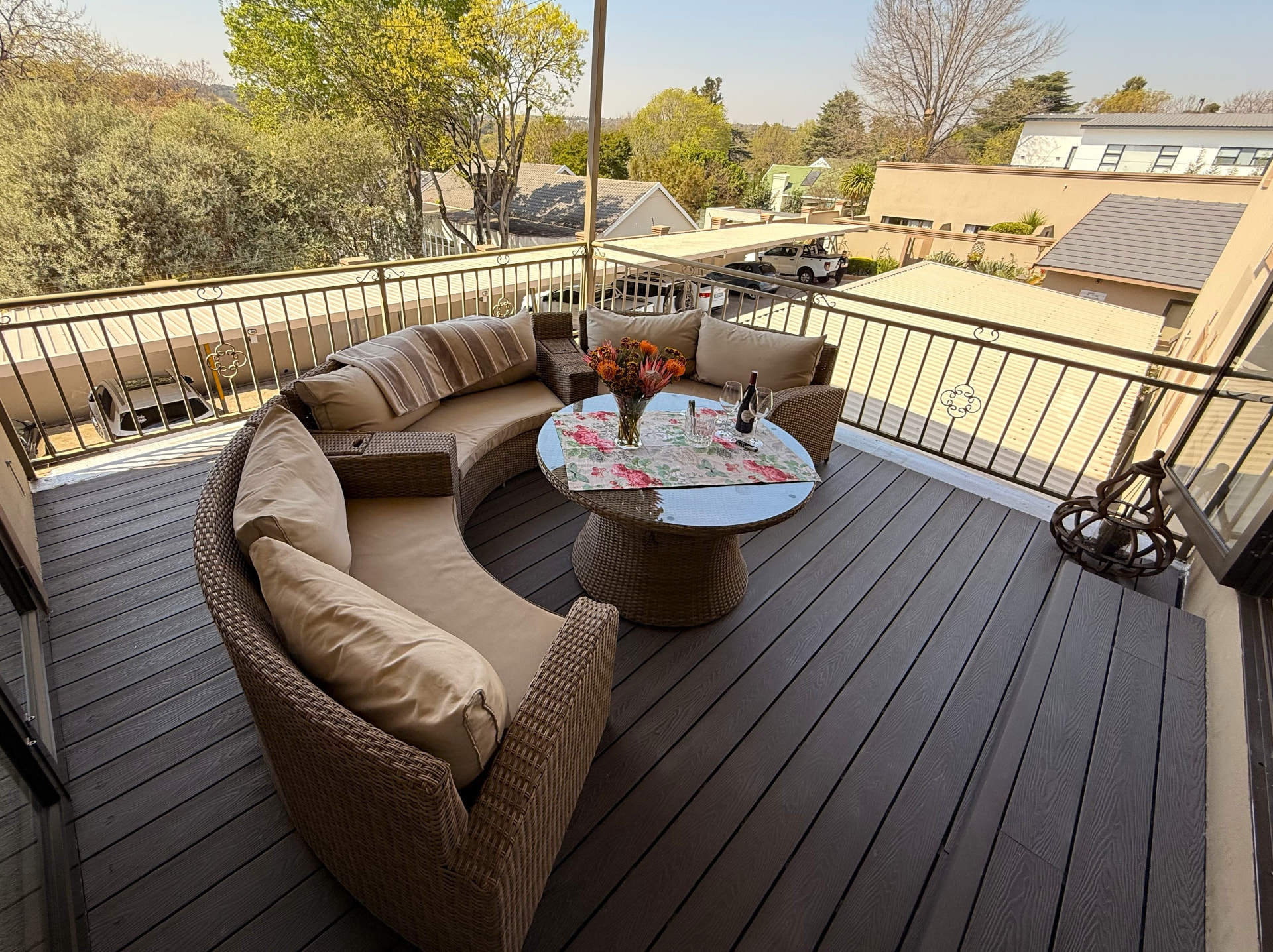 Covered private patio with curved wicker lounge seating, a flower-decorated table and a leafy outlook