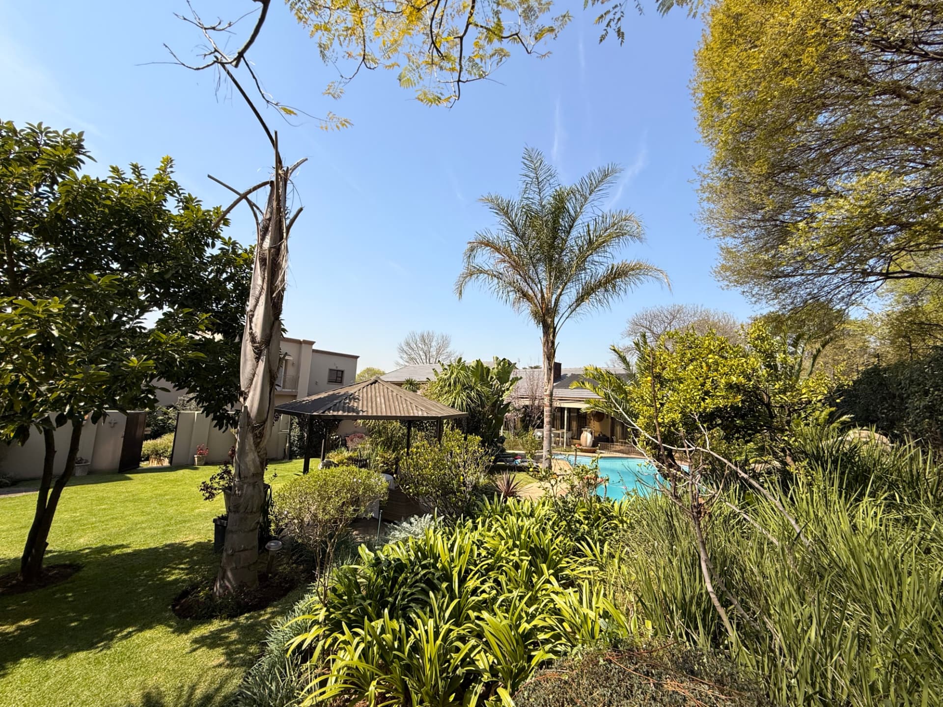 Wide view of the Dunton garden with lawns, mature trees, the gazebo and the pool beyond