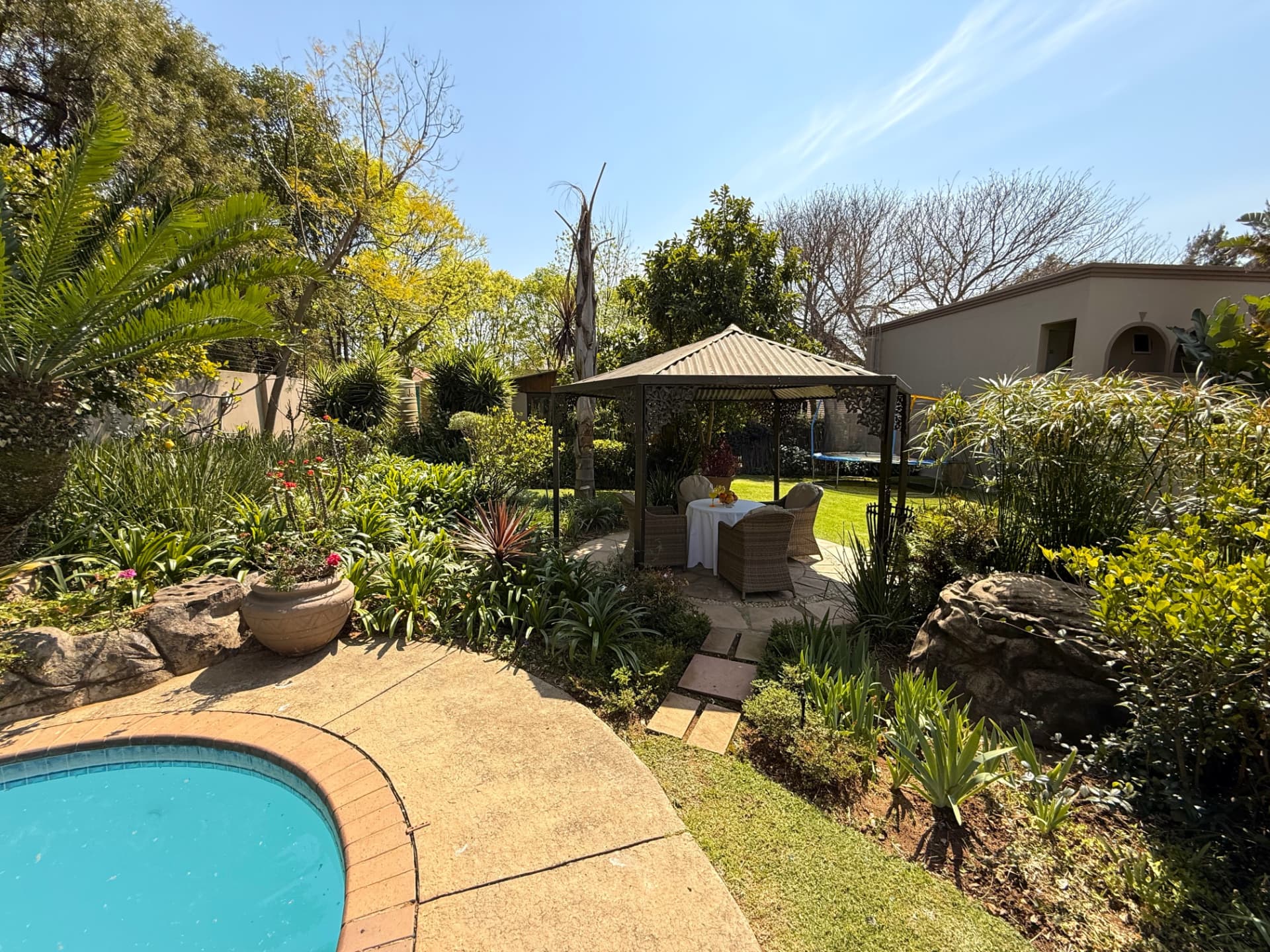 The pool edge at Dunton with the garden gazebo, landscaped beds and an outdoor table setting