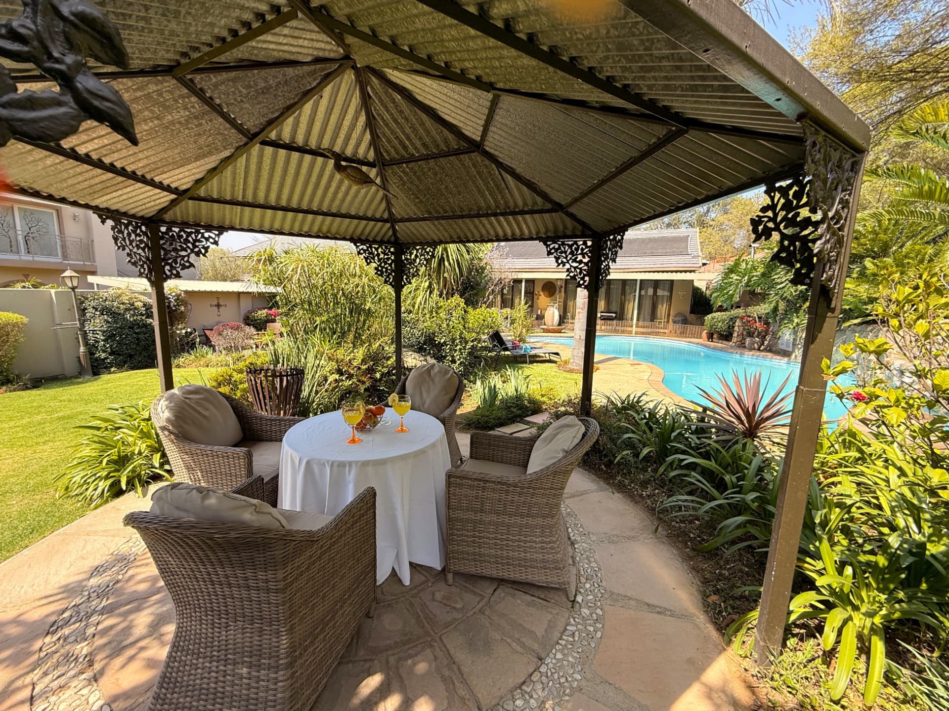 The wrought-iron gazebo at Dunton with cushioned wicker seating, the lawn on one side and the pool on the other