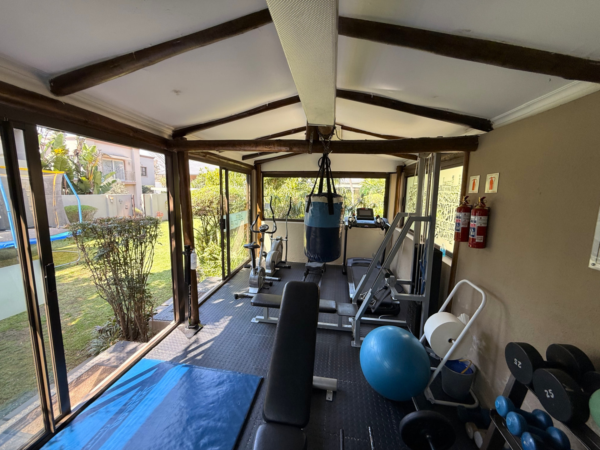Interior of the Dunton Guest House gym with a punch bag, treadmill, exercise bikes, benches and dumbbells, with sliding doors open to the garden