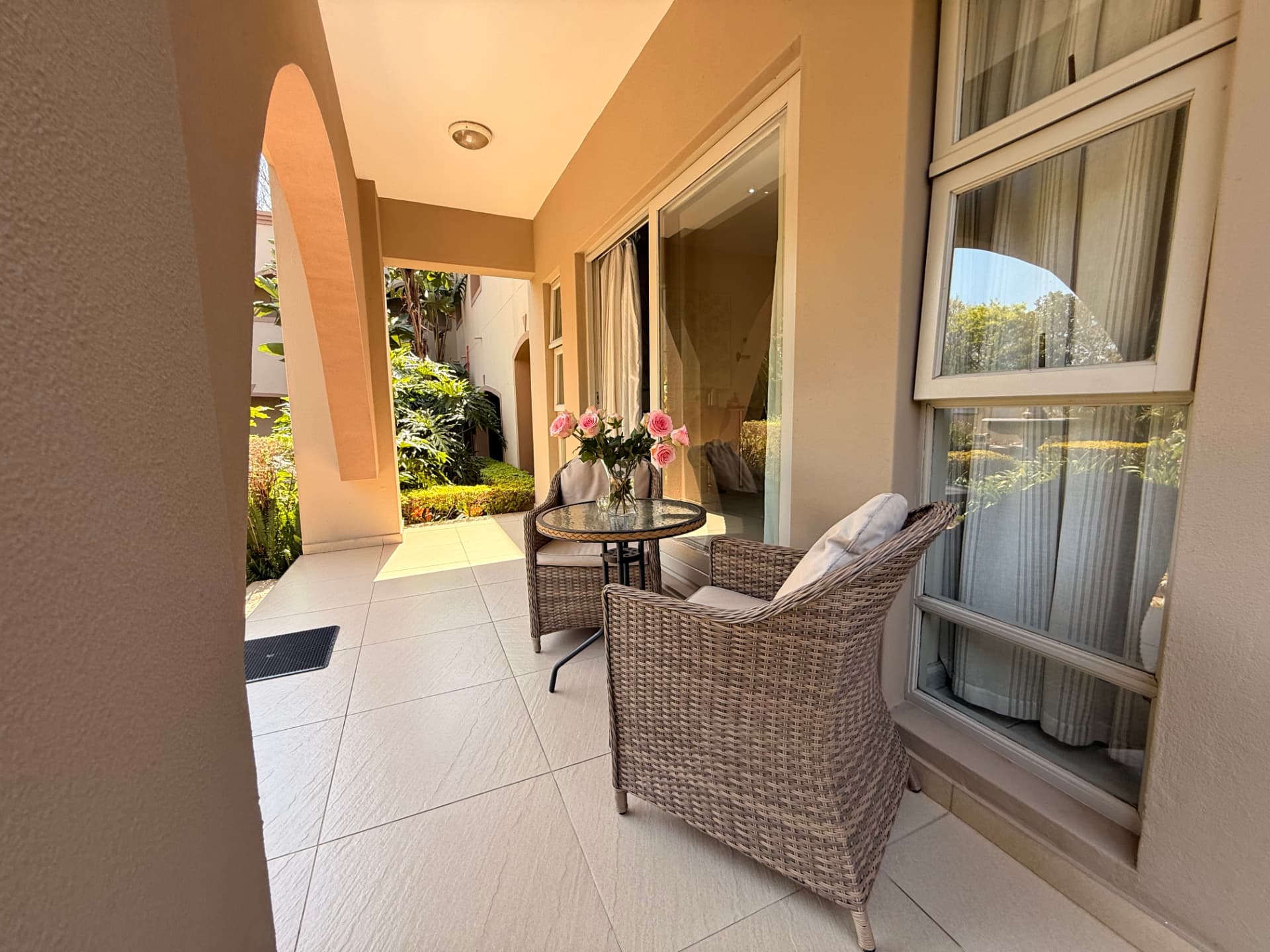 Covered guest patio at Dunton with wicker chairs, a flower arrangement and a landscaped courtyard beyond