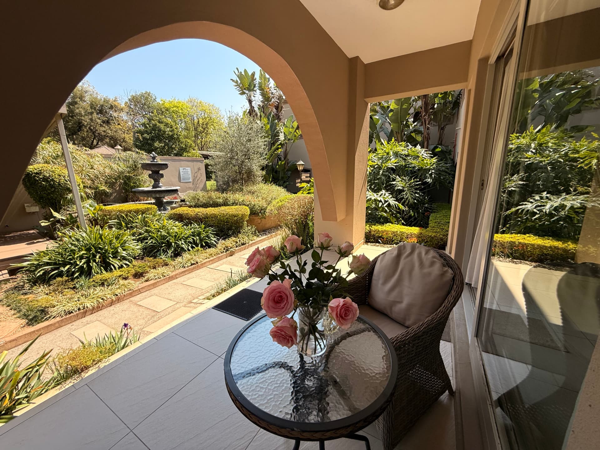 Covered patio at Dunton with wicker seating, a water feature, flowers and garden views
